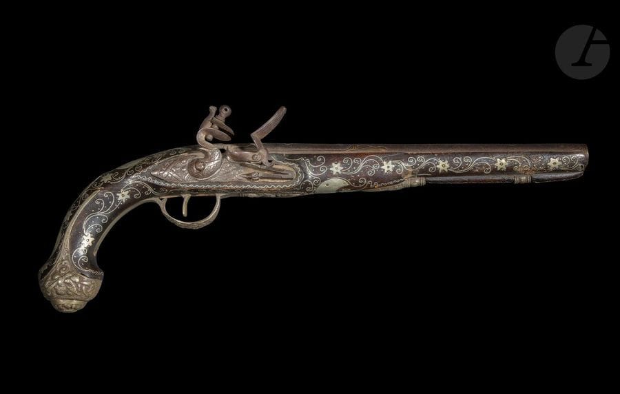Pistolet à silex, Empire ottoman, daté 1175H [?] / 1761
Canon rond en acier sur le dessus, damasquiné à l’or de décors végétaux dans des cartouches fleuronnés. Entre les deux fleurons, petit cartouche rectangulaire champlevé de la date 1175H [ ?] / 1761, et dans le fleuron proche du chien, petit médaillon circulaire champlevé de caractères arabes, probablement la marque du fabriquant. Platine à silex à garniture d’acier gravé d’un décor végétal et chien col de cygne. Crosse en bois à long fut à décor de rinceaux floraux et de deux croissants damasquinés d’argent disposés autour d’une plaque d’argent à décor végétal. Pommeau rond à oreilles couvert de plaques d’argent à décor végétal moulé tout comme le pontet.
Longueur : 47 cm
État : légers accidents, silex manquant.

A flintlock pistol, Ottoman Empire, dated

Ancienne collection de Monsieur A. Jacob (1942-1988)
Lots de 340 à 351
Alain jacob (1942-88), grand passionné et spécialiste des armes blanches, auteur d’une thèse sur les cimeterres turco-iraniens, travailla au Musée du Louvre et au Musée de l‘Armée avant de devenir rédacteur en chef de la revue d’antiquités ABC, membre fondateur de l’Union Française des Experts, il en devint ensuite vice-président. Il est l’auteur d’une série d’articles très documentés et d’ouvrages de référence sur les armes blanches du monde islamique et de l’Afrique : Armes blanches de l’Afrique Noire, Paris : 1974 ; Les armes blanches du monde islamique, Paris : 1985.