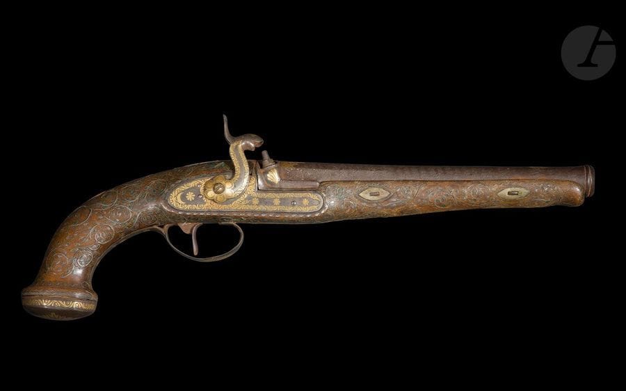 Pistolet à silex, Empire ottoman, XVIIIe siècle
Canon rond à pans à décors damasquinés d’or de fleuron végétal et motif solaire sur fond d’acier damassé. Platine à silex, chien col de cygne damasquinés à l’or de frises de palmettes, rosettes, croissants de lune, coquillages, motifs rayonnants ou fleuronnés. Crosse en bois à long fut à décor de rinceaux végétaux incrustés d’argent et déployés autour d’une amande dorée. Pommeau à calotte plate damasquinée à l’or d’une frise de palmettes et d’un motif rayonnant repris sur le pontet flanqué de trois rosettes et d’un fleuron damasquinés.
Longueur : 39,5 cm
État : traces d’oxydation, quelques incrustations manquantes, chien fragmentaire.

A flintlock pistol, Ottoman Empire, 18th century

Ancienne collection de Monsieur A. Jacob (1942-1988)
Lots de 340 à 351
Alain jacob (1942-88), grand passionné et spécialiste des armes blanches, auteur d’une thèse sur les cimeterres turco-iraniens, travailla au Musée du Louvre et au Musée de l‘Armée avant de devenir rédacteur en chef de la revue d’antiquités ABC, membre fondateur de l’Union Française des Experts, il en devint ensuite vice-président. Il est l’auteur d’une série d’articles très documentés et d’ouvrages de référence sur les armes blanches du monde islamique et de l’Afrique : Armes blanches de l’Afrique Noire, Paris : 1974 ; Les armes blanches du monde islamique, Paris : 1985.