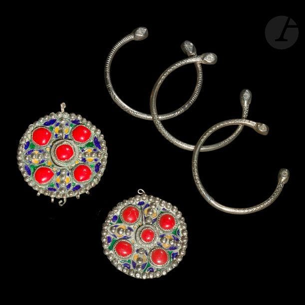 Paire de fibules rondes, tabzmit, Algérie, Grande Kabylie, Beni Yenni, début XXe siècle
Métal argenté émaillé en polychromie et cabochons rouges à décor de motifs géométriques émaillés jaune, vert et bleu sertis de perles argentées.
Diamètre : 7,5 cm
On y joint trois bracelets ouverts en métal argenté ciselé de motifs géométriques, Afrique du Nord, début XXe siècle
Diamètre : 8 cm

A pair of round silver fibulae, tabzmit, Algeria, Great Kabylia, Beni Yenni, early 20th century