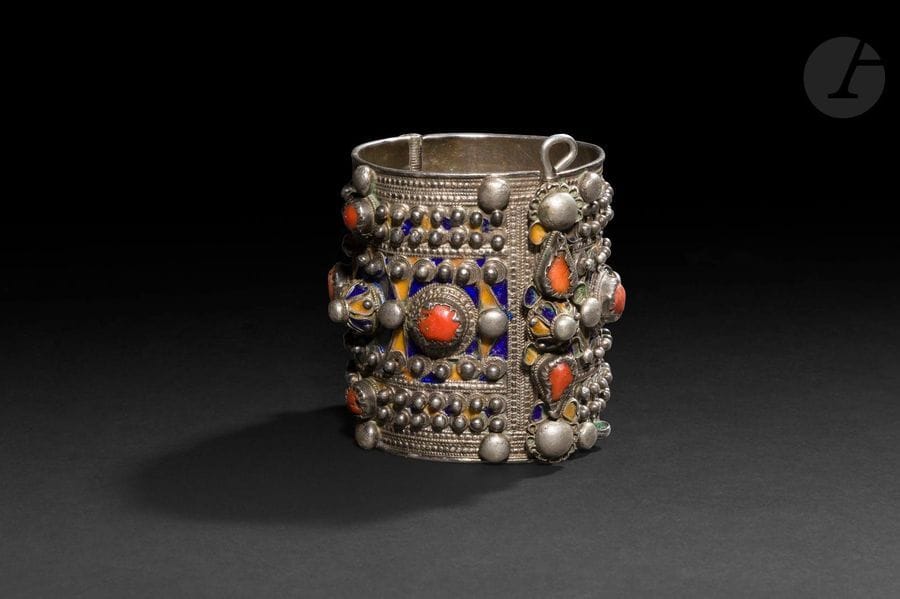 Large bracelet articulé, Algérie, Grande Kabylie, Beni Yenni, début XXe siècle
En argent émaillé polychrome à décor géométrique perlé et serti de cabochons de corail scandés de cabochons émaillés. Charnière ouvrante.
Hauteur : 7 cm ; Diamètre : 7 cm ; Poids brut : 246,9 g

A silver bracelet, Algeria, Great Kabylia, Beni Yenni, early 20th century