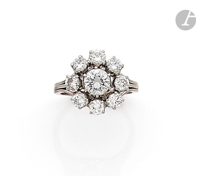 Bague en or gris 18K (750) et platine, ornée d’un diamant rond de taille brillant entouré de 8 diamants ronds plus petits. Travail français des années 1960. Tour de doigt : 48. 
Poids brut : 7,5 g (accident à l’anneau)