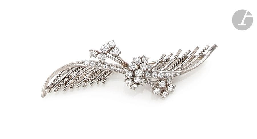Broche en fils d’or gris 18K (750) lisse et torsadé dessinant une plume stylisée agrémentée de fleurettes serties de diamants ronds. Longueur : 6,2 cm environ. 
Poids brut : 10,4 g