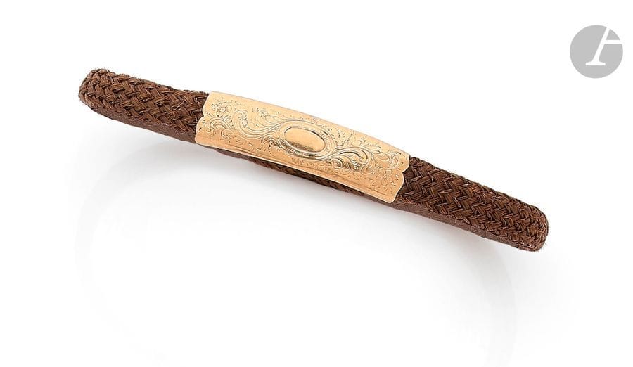 Bracelet en cheveux tressés, orné d’un motif en or 18K (750) ciselé de feuillages. Travail français de la seconde moitié du XIXe siècle. Longueur : 23,3 cm environ. 
Poids brut : 6,5 g