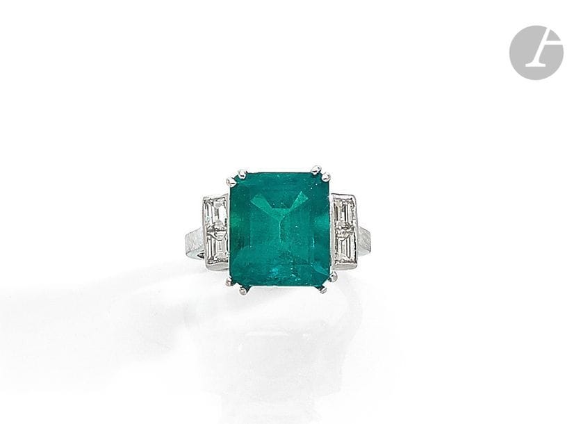 Bague en or gris 18K (750), ornée d’une émeraude pesant 6,08 cts de forme rectangulaire à pans coupés, épaulée de diamants calibrés. Tour de doigt : 53 / 54. 
Poids brut : 5,6 g
 L’émeraude accompagnée d’un rapport LFG (2019) attestant selon son opinion : origine Colombie, présence d’huile et de résine (choc).