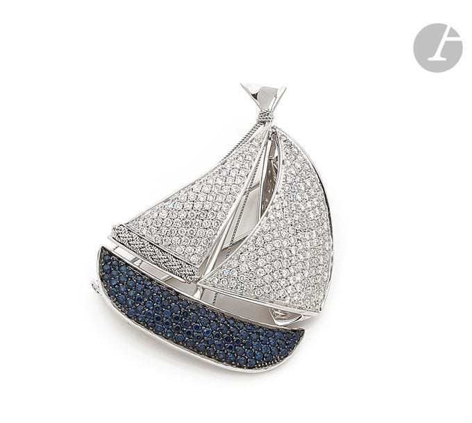 Pendentif en or gris 18K (750) formant un voilier, la coque pavée de saphirs, les voiles parées de diamants ronds, coulissant sur une fine chaîne d’or gris 18K. Le pendentif portable en broche-clip. Dimensions : 5 x 3,9 cm environ. 
Poids brut : 26,2 g