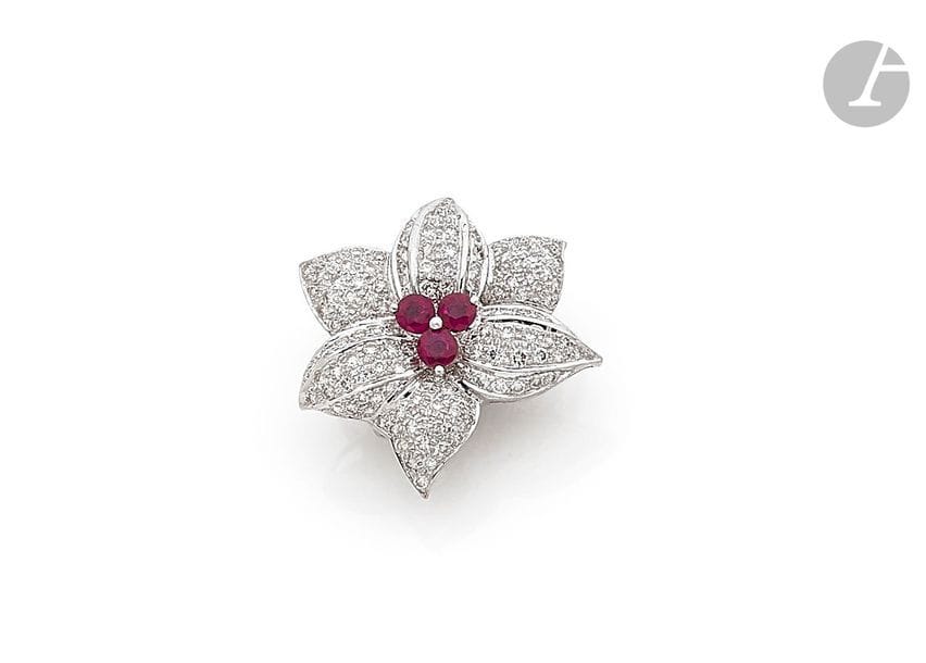 Clip de revers fleur en or gris 18K (750), les pétales pavés de diamants ronds, le pistil piqué de trois rubis. Hauteur : 3 cm environ. 
Poids brut : 8,7 g (peut se porter en pendentif)