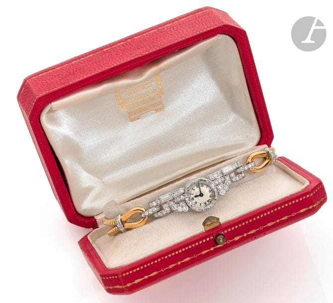 CARTIER. Vers 1949
N°29892 - 08597
Montre bracelet pour femme en platine (950), boîtier asymétrique serti de diamants, lunette sertie de diamants taille baguette, cadran blanc index chiffres romains formant les heures, aiguilles en acier bleui, mouvement à remontage mécanique signé EWC&C (fonctionne), bracelet en or jaune 18K (750) de type tubogaz.
Cadran, boîtier, mouvement signés.
La montre est accompagnée de son écrin et d’une photocopie de la facture d’achat.
Poids brut : 29,6 g
Longueur : 17,7 cm