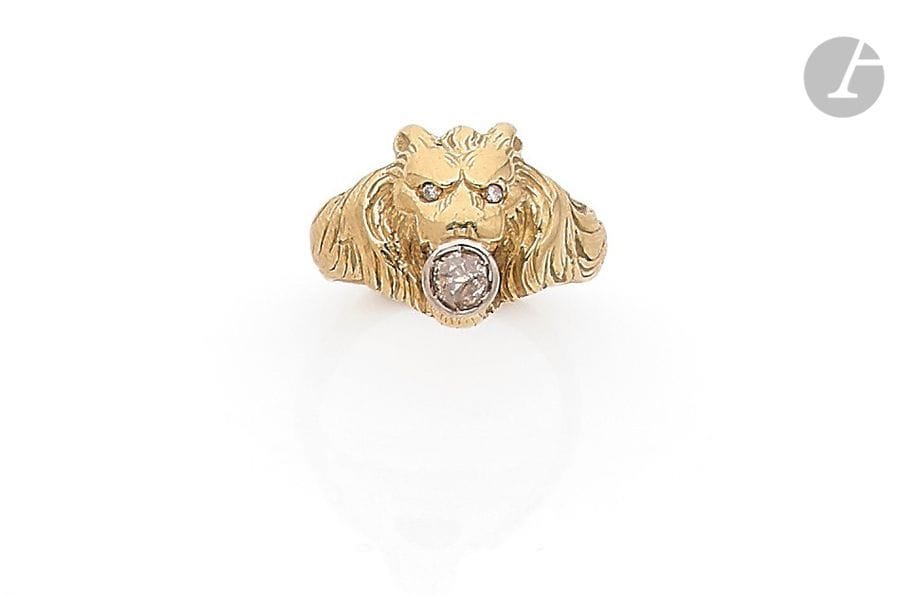 Bague en or 18K (750), ornée d’une tête de lion tenant dans ses crocs un diamant de taille ancienne, ses yeux piqués chacun d’un diamant rond. Travail du début du XXe siècle. Tour de doigt : 56. 
Poids brut : 11,3 g (choc)