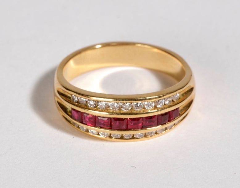 Bague en or 18K (750), ornée d'une ligne de rubis calibrés entre deux lignes de diamants ronds. Tour de doigt : 54. Poids brut : 5,3 g