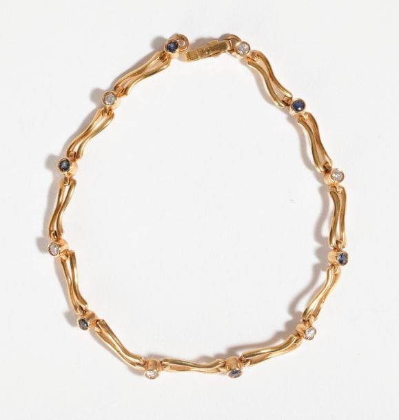 Bracelet en or 18K (750), articulé de maillons sinueux scandés de diamants et de saphirs ronds. Longueur: 18,8 cm environ. Poids brut : 9,1 g