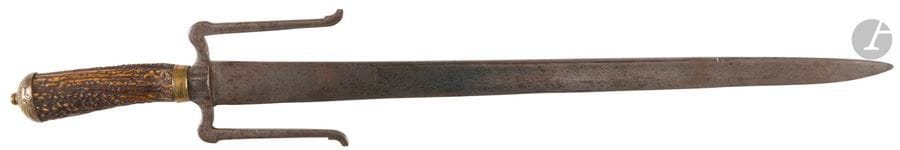 Couteau de vénerie.
Poignée en bois de cerf. Monture en laiton. Garde en fer à deux longs quillons courbés vers le bas. Lame à dos plat, contre tranchant et pans creux, gravée au talon.
E.M. XVIIIe / XIXe siècle (composite).

