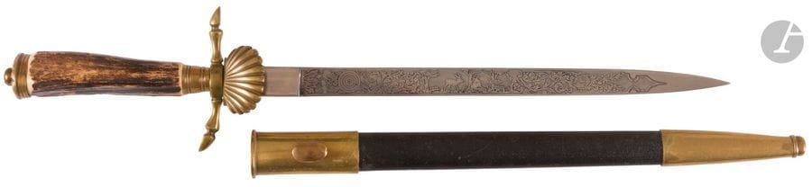Couteau de vénerie allemand. 
Poignée en bois de cerf. Monture en laiton, garde à deux quillons en patte de biche. Clavier en coquille. Lame droite « Horster & Co », gravée de sous-bois et trophées de chasse. 
Fourreau recouvert de chagrin à deux garnitures en laiton. 
B.E. XXe siècle. 

