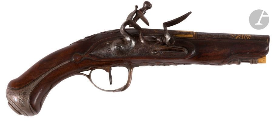 Pistolet à silex de demi-arçon d’officier. 
Canon rond, à pans au tonnerre, bleui, gravé et doré de motifs feuillagés et soleil. Platine et chien à corps rond, signé autour du ressort de batterie « MANUFACTURE DE TULLE ». Garnitures en argent ciselé. Calotte à longue oreille gravé d’oiseaux et de rinceaux feuillagés et de rocaille. Pontet gravé d’armoiries sous couronne de comte, soutenues par des griffons. Baguette en bois à embout en ivoire. 
Longueur : 25 cm
B.E. Vers 1760. 

