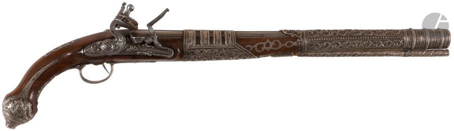 Grand pistolet à silex marocain. 
Long canon rond de fort calibre à méplats et nervures au tonnerre. Platine et chien col de cygne à corps plats, ciselée de rinceaux feuillagés. Bassinet en fer à pare étincelles. Couvre bassinet décoré en suite. Belles et grandes garnitures en argent découpé, à décor repoussé d’anneaux striés, de rinceaux feuillagés et suite de perles. Monture en noyer à long fût orné de plaques d’argent à jours, découpées et incrustées. Calotte enrichie d’une pièce de corail. Baguette en bois à long embout en argent.
B.E. Milieu du XIXe siècle.
Longueur : 62 cm

