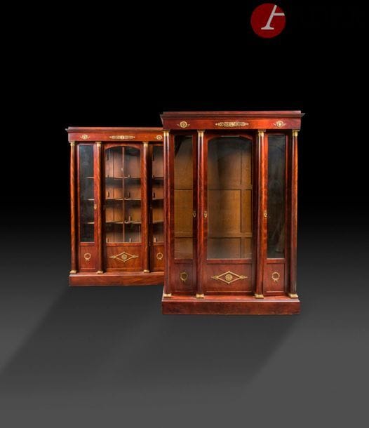 Paire de bibliothèques en acajou flammé, la façade à quatre colonnes colossales ouvrant à trois portes vitrées et reposant sur une plinthe surmontée de rosace, losange et couronne de bronze doré.
Style Empire (accidents).
H : 235 cm, L : 158 cm, P : 50 cm