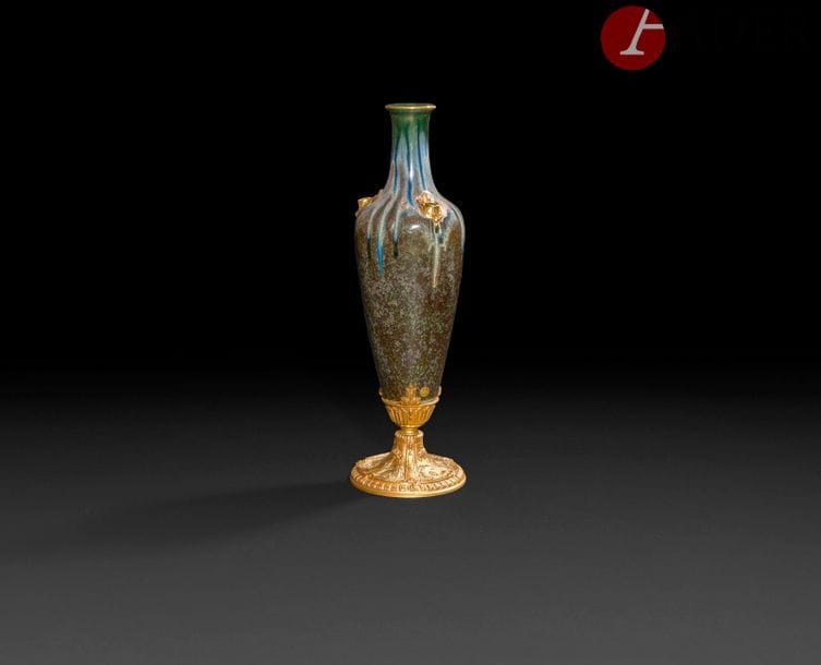 Vase d’ornement formant pique-fleurs, en porcelaine de la manufacture Pillivuyt, à décor émaillé de coulures grise, roses et bleu sur fond gris vert, reposant sur un piédouche en bronze doré à décor de rinceaux et fleurs ; cachet de la maison Louchet ciseleur à Paris.
Fin du XIXe siècle.
H : 34 cm