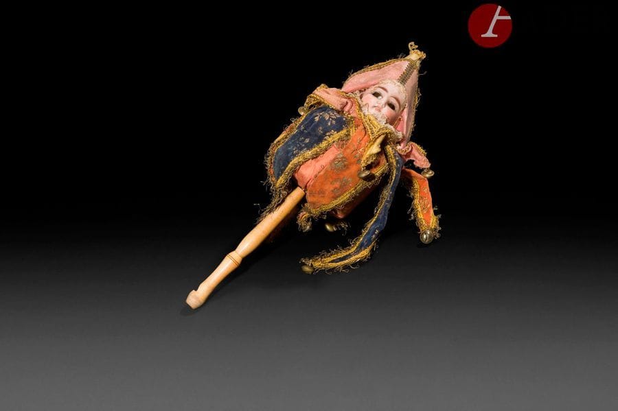 Marotte à sifflet, tête en porcelaine (manquent les yeux), bouche ouverte sur une rangée de dents, costume à grelots et chapeau, manche en bois se terminant par un sifflet.
H : 35 cm