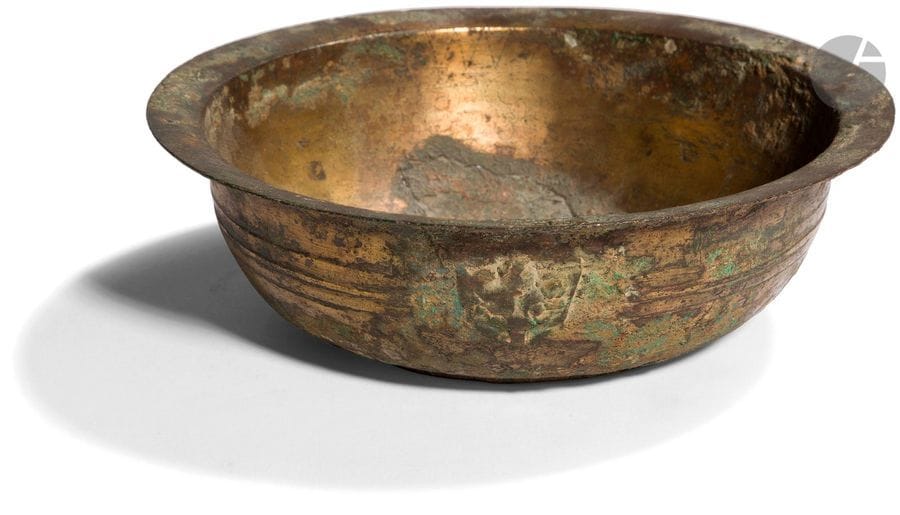 CHINE - époque HAN (206 av. JC - 220 ap. JC)
Bol en bronze à traces de dorure à bordure évasée, la panse ornée d’un ourlet, les côtés flanqués de deux anses formant têtes de taotie. (Petits manques et restauration).
Diam. 16,9 cm