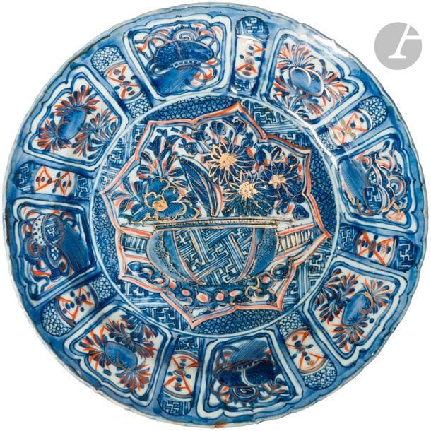 CHINE - XVIIe siècle
Assiette Kraak en porcelaine émaillée en bleu sous couverte et rehaut d’or et de rouge de fer, à décor central d’une vasque fleurie, de panneaux de fleurs et symboles bouddhiques en réserve. (égrenures en bordure et restauration). 
Diam. 29,1 cm