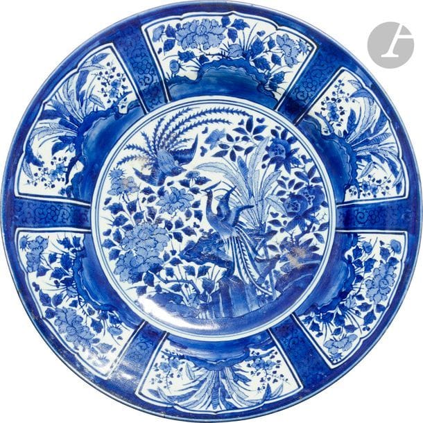JAPON, Fours d’Arita - Fin XVIIe siècle
Important plat dit Kraak en porcelaine décorée en bleu sous couverte d’un couple de paons parmi les pivoines et les bananiers, l’aile décorée de réserves de bananiers et pivoines.
Diam. 57 cm