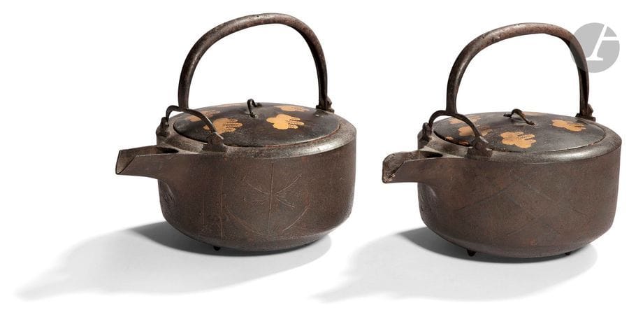 JAPON - Époque MEIJI (1868 - 1912)
Deux théières en fonte de fer, dit « tetsubin », coiffées de couvercles en bois laqué brun orné en laque or de fleurs de paulownia, l’une à décor en relief sur la panse de pins et de fleurs de prunus, l’autre de citrons digités dans leur feuillage. (Petits éclats et manques). 
H. 18 cm