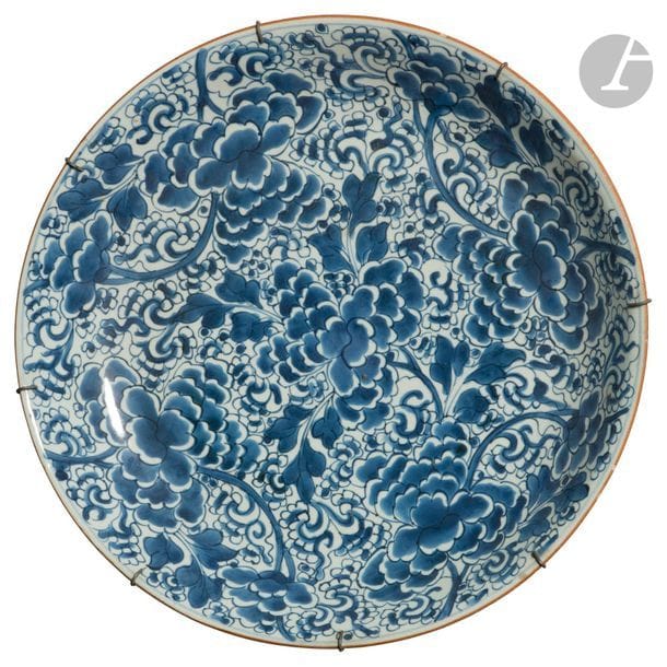 CHINE - Époque KANGXI (1662 - 1722)
Grande coupe en porcelaine blanche émaillée en bleu sous couverte de fleurs de chrysanthème parmi des rinceaux feuillagés mouvementés. (Fêlure). 
Diam. 38,4 cm