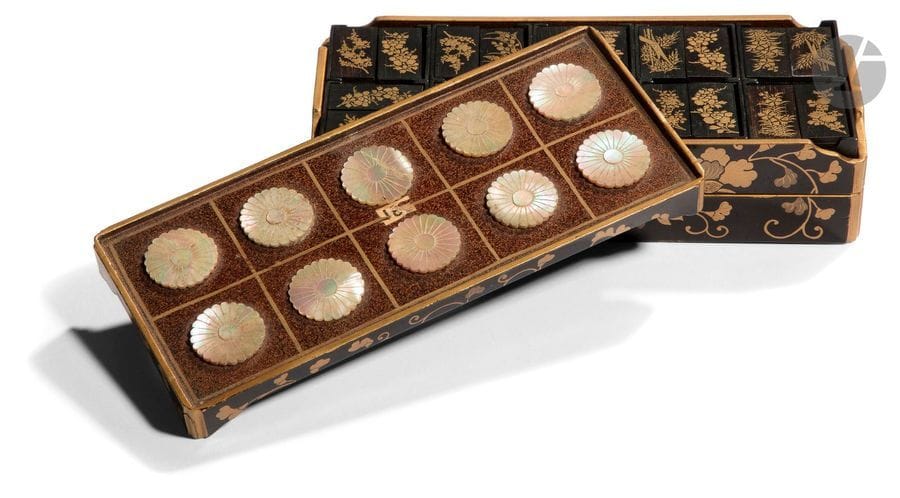 JAPON - Époque MEIJI (1868 - 1912)
Kobako à jeux et suzuribako rectangulaire à trois étages en laque noir à décor en laque or et kirigane de fleurs dans leurs rinceaux, la partie supérieure en laque nashiji ornée de fleurons de kiku en nacre. (Restaurations et petits sauts de laque).
15,5 x 4 x 7 cm