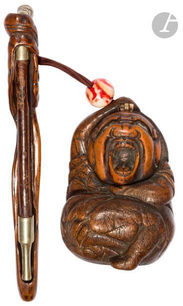 JAPON - Époque MEIJI (1868 - 1912)
Tonkotsu et kizeruzutsu en bois sculpté, en forme de Daruma se touchant le haut de la tête de sa main droite, la bouche grande ouverte, l’embout et la fin de la pipe en métal. L’ojime en verre rouge et blanc. (Usures). 
H. 10,5 cm ; kizeruzutsu : H. 20,6 cm