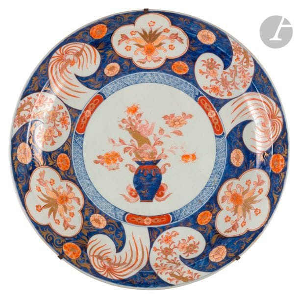CHINE - Époque KANGXI (1662 - 1722)
Plat rond en porcelaine émaillée polychrome dans le style dit « Imari », à décor central d’un chien de fô dans un vase, de médaillons polylobés et de spirales en réserve, ornés de fleurs et de phénix sur fond bleu.
Diam. 47 cm