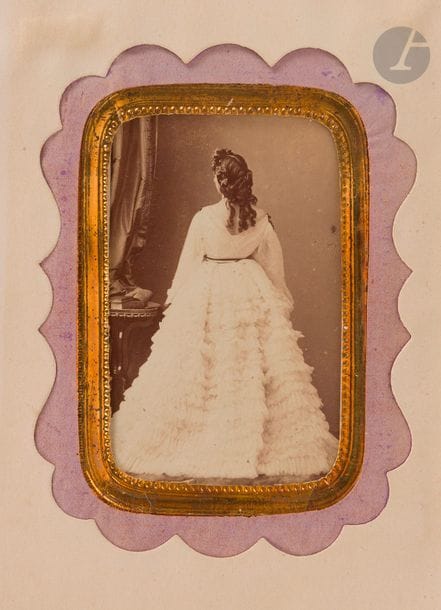 DELIONS (Anna).
Photographie sur papier albuminé, format carte de visite, vers 1860.

Superbe photo de Disdéri représentant Anna Deslions de dos. Cette dernière était une célèbre courtisane mondaine du Second Empire, appelée « la lionne des boulevards », qui devint une artiste célèbre grâce à sa beauté et à certains dons. Zola se serait inspiré en partie de sa vie pour son personnage de Nana.
La photo est présentée dans un bel encadrement doré et mauve.
