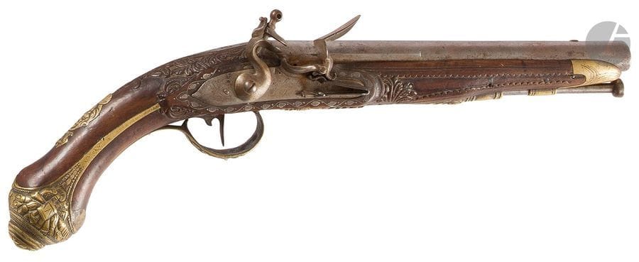 Pistolet d’officier pour l’export. 
Canon rond, à méplats au tonnerre. Platine (restes de signature) ceinturée d’une frise de feuilles d’argent incrusté et chien à corps rond. Garnitures en laiton fondu et ciselé à décor de feuillages et trophées. Crosse en noyer richement sculpté à décor feuillagé. 
A.B.E. Milieu du XIXe siècle.