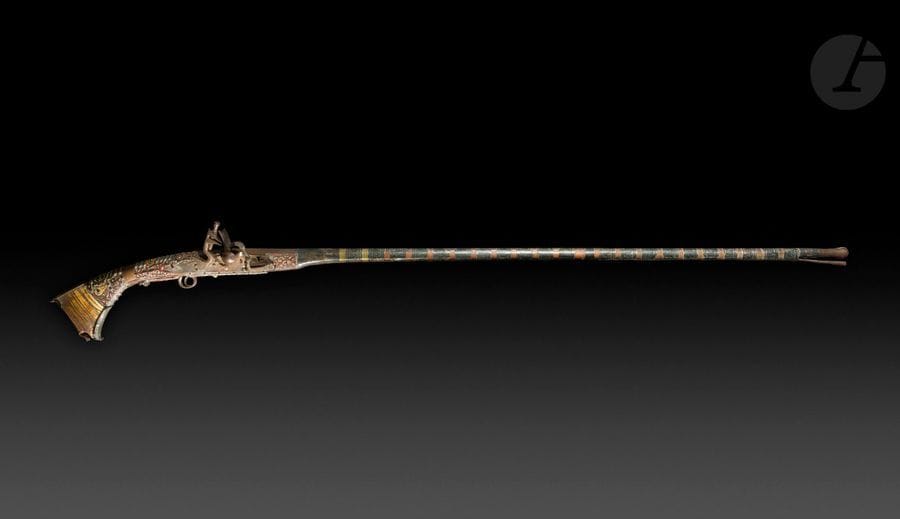 Grand fusil d’Afrique du Nord dit Moukalah

Long et fin canon rond et à pans tulipé à la bouche.
Platine à la Miquelet, garnitures en cuivre, fer et laiton. Crosse et fût entièrement recouvert de plaques d’argent à décor découpé et rehaussé de couleur rouge.
Talon de crosse en os de chameau avec plaque de couche (accidenté). 
Baguette en fer.
A.B.E. Accidents à la crosse.
Longueur : 161 cm

 Provenance :
Maréchal Alphonse Juin (1888-1967).

