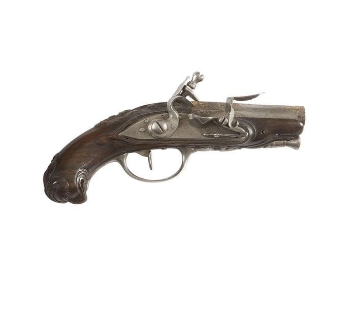 Petit pistolet de voyage à silex. 
Canon rond, à pans et méplat, décoré d’or. Platine à chien col de cygne à corps plats. Bassinet en fer. Garnitures et baguette en fer. Crosse en noyer sculpté à tête d’aiglon.
Longueur : 12 cm
B.E. Vers 1780-1800.