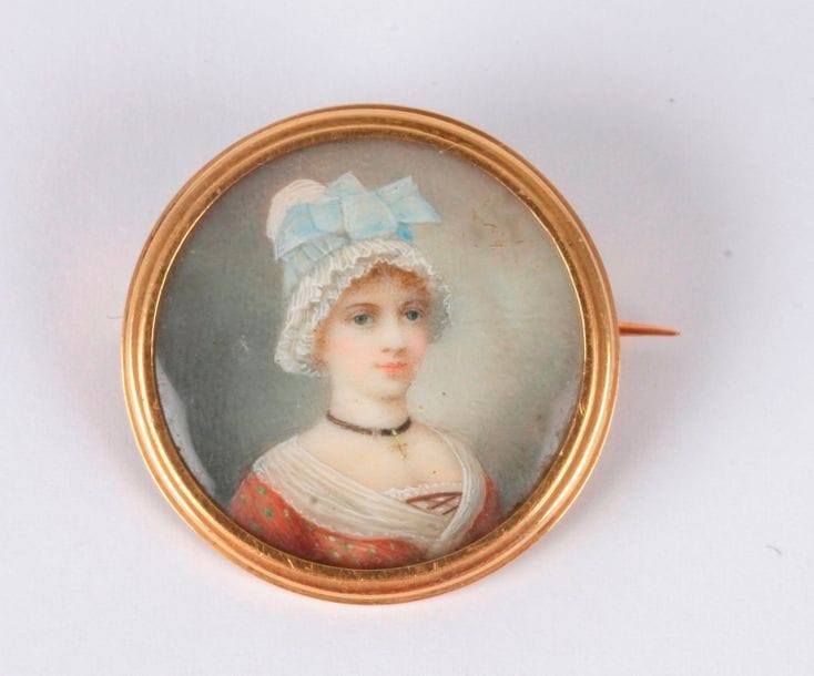 Jeune femme à la coiffe de dentelle ornée d'un gros nœud bleu, croix au cou attachée à un ruban noir, robe marron à pois verts, guimpe blanche

Miniature vers 1900, sur une petite broche ronde en or, diam. 2,7 cm

Poids total : 7,10 g