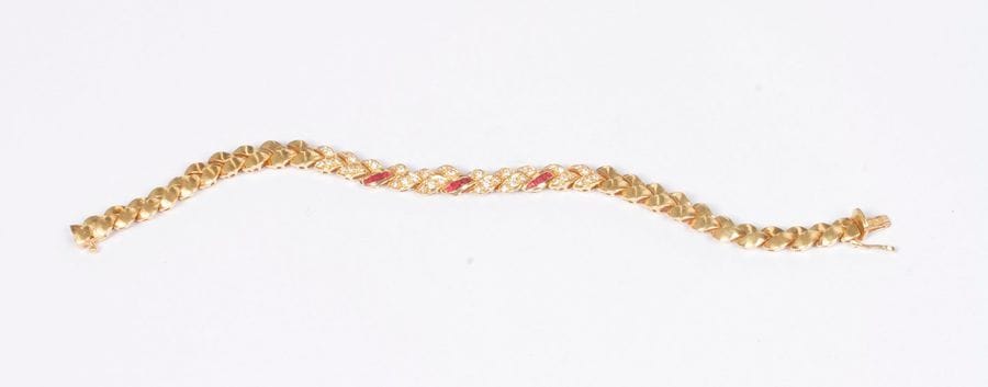Bracelet en or 18K (750), articulé de maillons en épis, ceux du centre agrémentés de diamants ronds ou de rubis calibrés. Longueur : 17,7 cm environ. Poids brut : 25,5 g