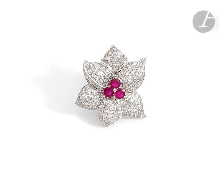 Clip de revers fleur en or gris 18K (750), les pétales pavés de diamants ronds, le pistil piqué de trois rubis. 
Hauteur : 3 cm environ. 
Poids brut : 8,7 g (peut se porter en pendentif)
