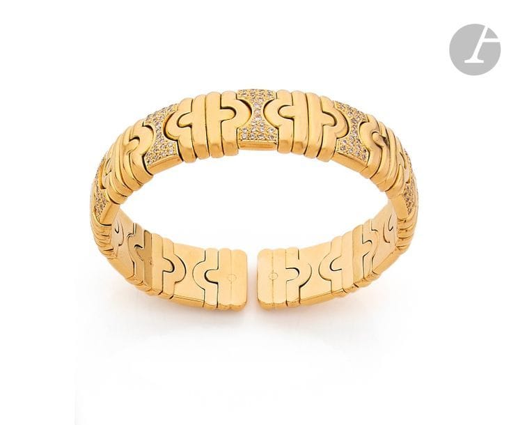 Bracelet torque orné de motifs en or jaune 18K (750) imbriqués, certains agrémentés de diamants ronds. 
Dimensions : 1,3 x 15,8 cm environ. 
Poids brut : 78,7 g (âme en acier)