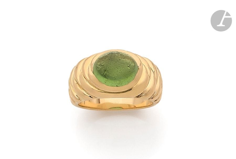 Large bague en or 18K (750) façonnée en « pomme de pin », sertie d’un péridot cabochon. 
Tour de doigt : 66. 
Poids brut : 23,1 g (à repolir)