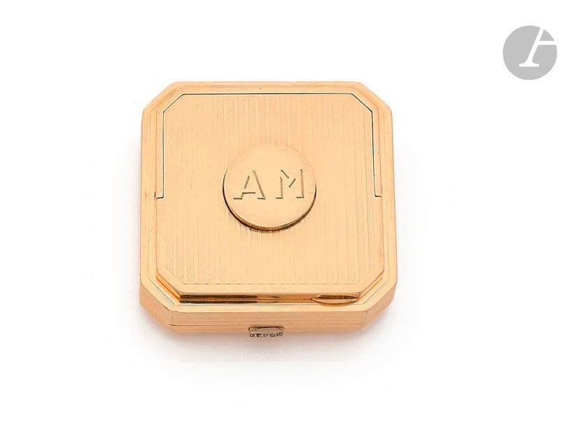 CARTIER
Poudrier octogonal en or 14K (585) guilloché de bandes et méplats, le couvercle orné d’une pastille chiffrée (AM) découvrant une cachette pour rouge à lèvres, il recèle un miroir basculant ainsi qu’un compartiment à poudre libre muni d’un tamis incorporé, le poussoir agrémenté de diamants taillés en roses. Signé. Travail des années 1930. 
Dimensions : 4,7 x 4,7 x 1,5 cm environ. 
Poids brut : 102,5 g (piqûres)