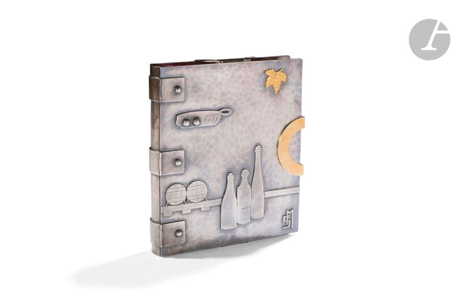 JEAN DESPRÉS (1889-1980)
Livre de cave d’un vigneron
Rare jaquette de livre en métal argenté.
La façade articulée au plat présentant un décor en applications de bouteilles, de tonneaux et d’un taste-vin en métal argenté ; un pampre de vigne en métal doré également en application ; le tout sur fond à large martelage.
Le fermoir en métal doré.
Les charnières aux fixations en demi-sphères.
Un motif monogramme M. S. en application en bas à droite du plat de couverture.
La 4e de couverture à la surface à large martelage.
Signée du cartouche Jean DESPRÉS en application sur la 3e de couverture.
Plat de couverture : 28,3 x 24 cm
Épaisseur : 3,8 cm
