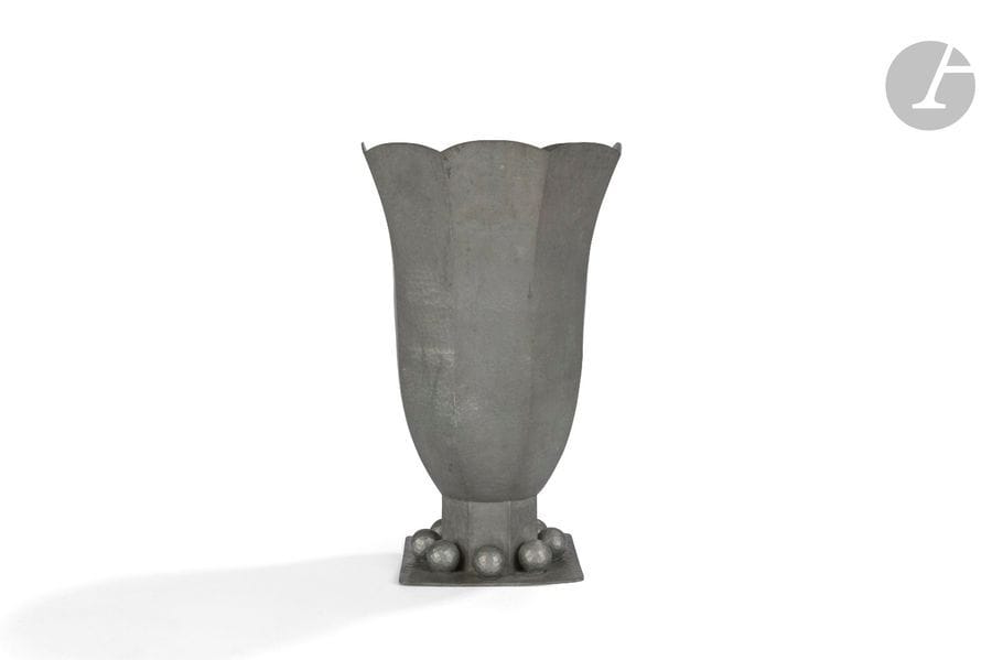 JEAN DESPRÉS (1889-1980)
Tulipe et sphères, pour M. Gaston Gaudaire, 1947
Haut vase cornet à facettes reposant sur une terrasse carrée.
Épreuve en dinanderie d’étain montée au marteau et à surface entièrement martelée.
Le corps du vase, terminé en découpe sur sa partie haute, est reçue par une base octogonale accueillie par la terrasse enrichie de huit importantes sphères facettées.
Signé J. DESPRÉS à la pointe sur la terrasse et inscrit : La Fédération des Sociétés Musicales de l’Yonne à Monsieur Gaston Gaudaire son Fondateur et Président 1907-1947, sous la base.
Hauteur : 34,5 cm