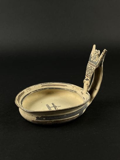 Kyathos, whose handle depicts a stylized...