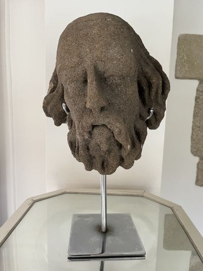 Carved granite head of a saint. Oval-shaped,...