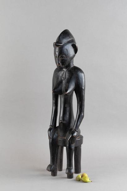 A female figurine depicted sitting on a stool....