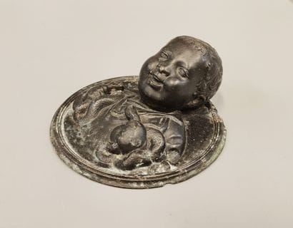 Patinated metal medallion in the round featuring...