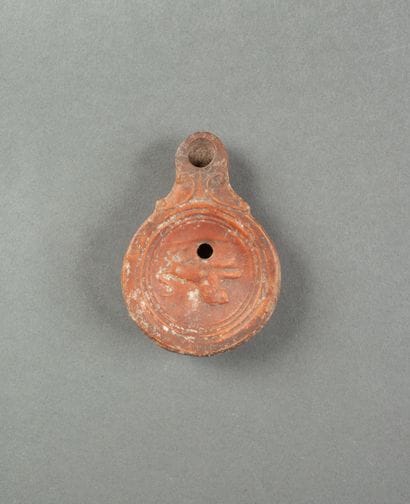 A red terracotta oil lamp with a scrolled...