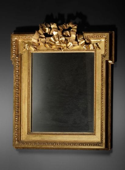 Miroir en bois doré à frise de d'oves surmontée...