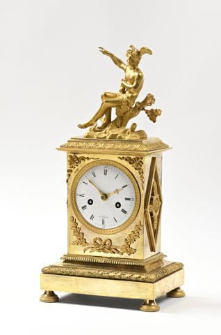 A gilded bronze clock surmounted by a seated...