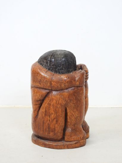 Wood sculpture of a seated, curled-up figure....