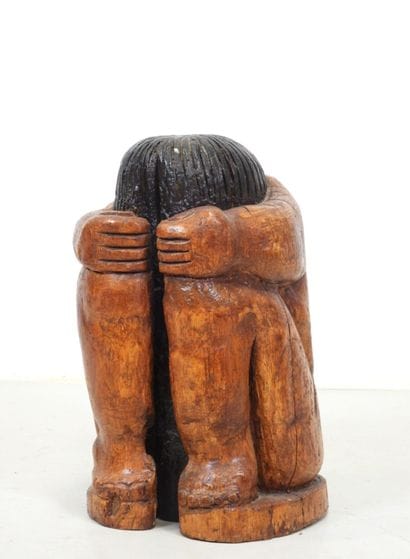 Wood sculpture of a seated, curled-up figure....